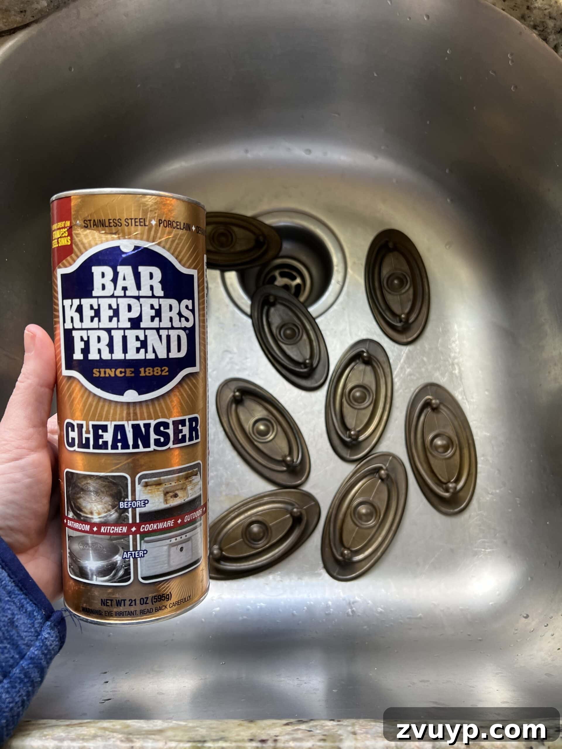 Close-up of a hand scrubbing metal furniture hardware with a toothbrush and Bar Keepers Friend