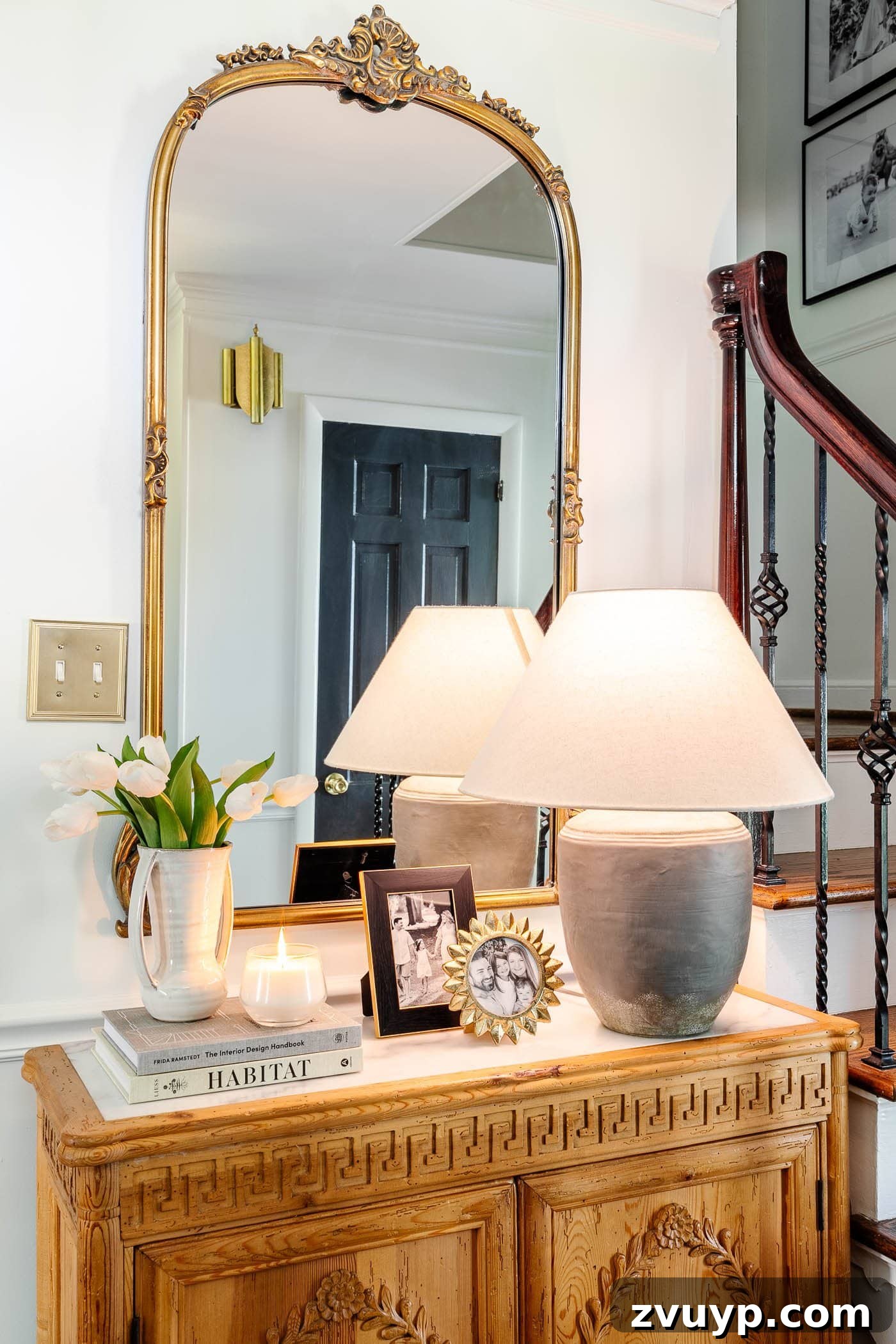 Pro Entry Table Styling: Your Step-by-Step Guide to a Stunning Entryway 3 entry table decor in a foyer with gold mirror, lamp, vase of tulips, candle, and picture frames on a carved wood cabinet