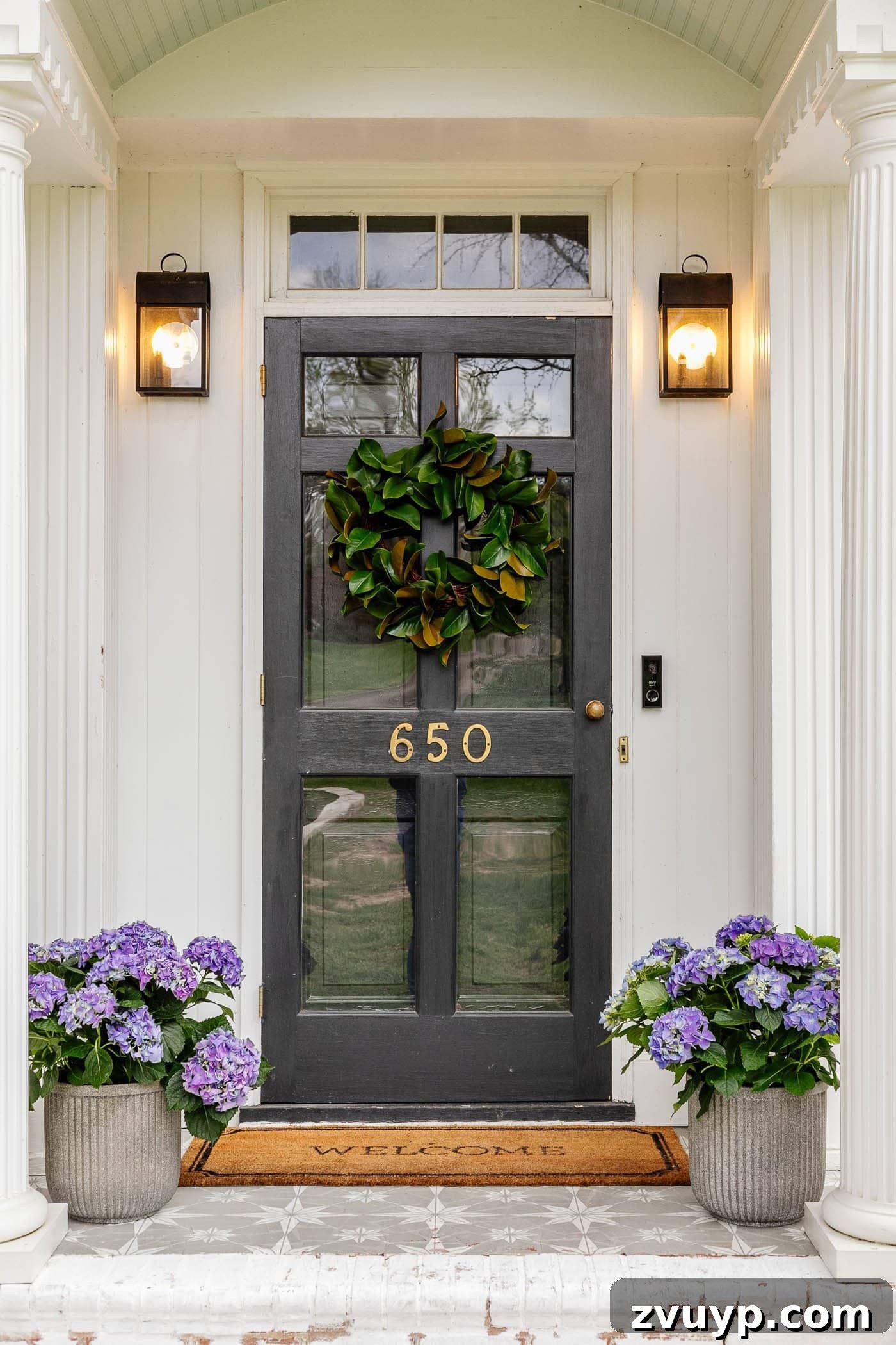 Tiny Porch, Big Curb Appeal: 6 Budget-Friendly Upgrades 10 black front door with white columns on a small front porch featuring a magnolia wreath, purple hydrangeas, and an extra-wide layered welcome mat