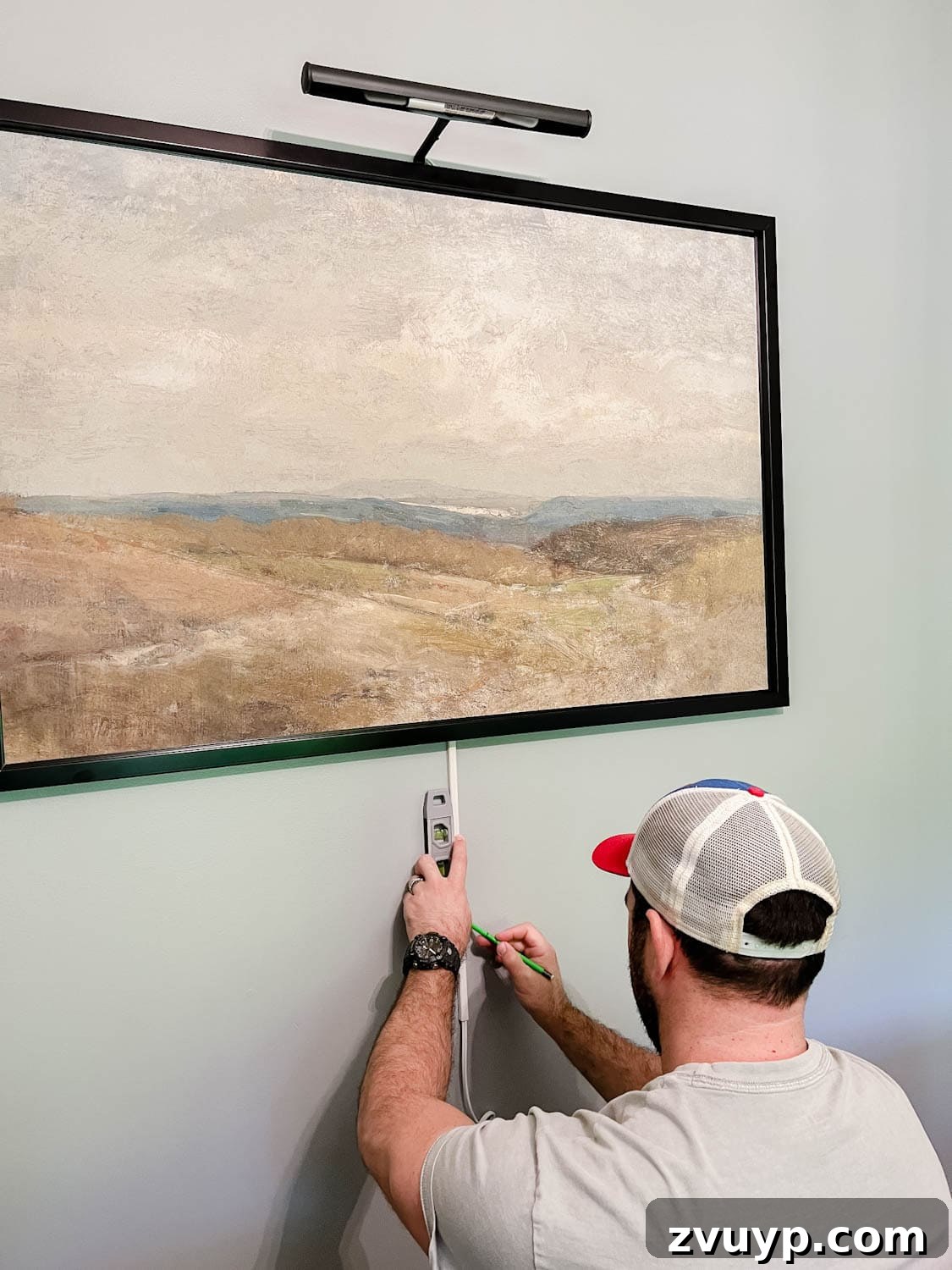 Illuminate Your Art Wirelessly: Picture Light Installation Guide 5 installing a picture light above a piece of art and wrapping cord in cord covers