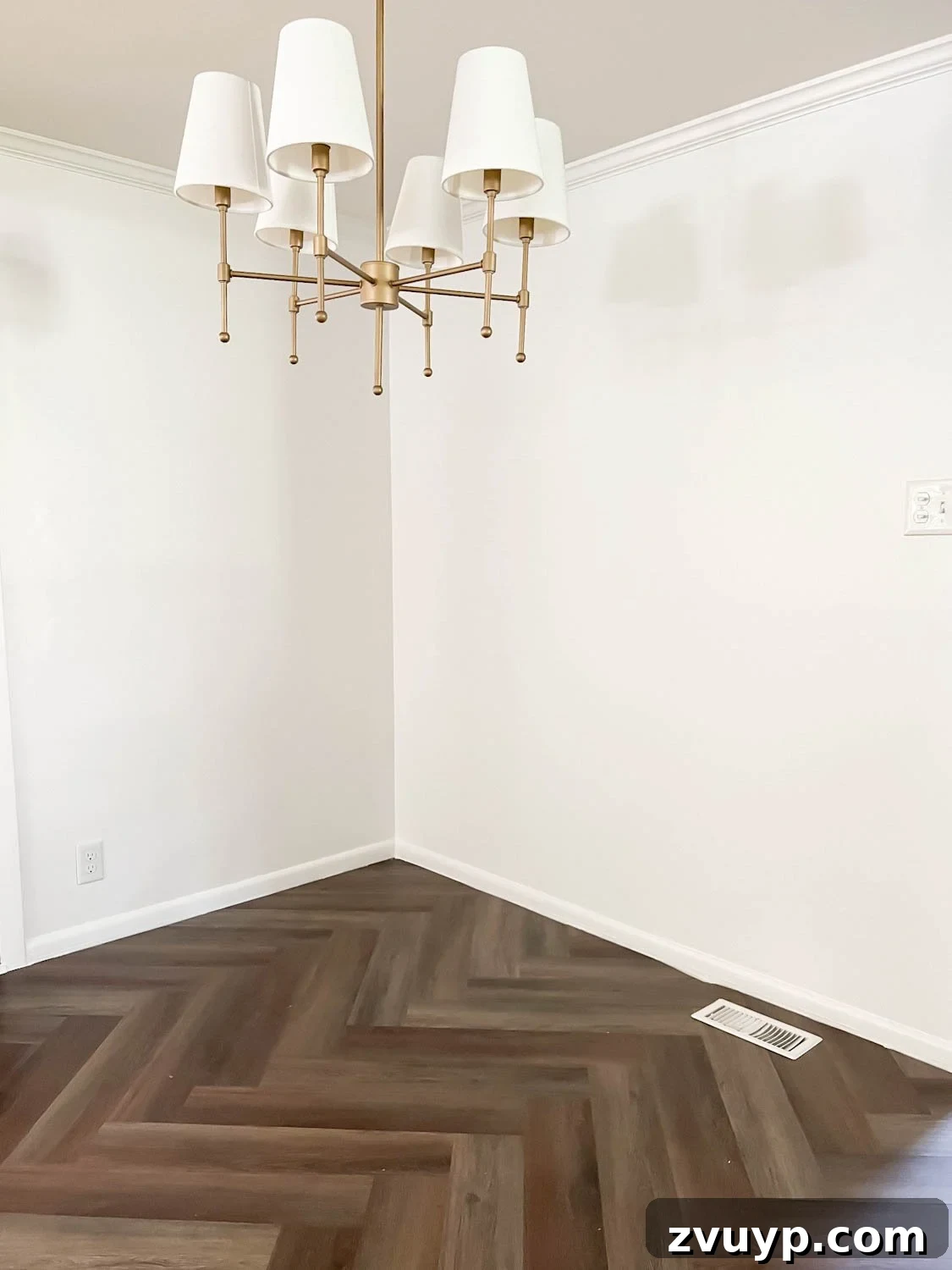 Corner Banquette Refresh and Hidden Vent Hacks 4 Corner of a breakfast nook featuring a linear chandelier, pristine white walls, herringbone LVP flooring, and a visible floor vent requiring redirection.