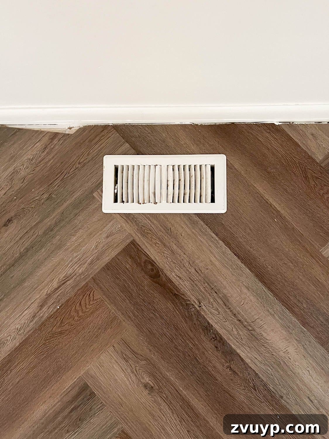Corner Banquette Refresh and Hidden Vent Hacks 5 Close-up view of a floor vent positioned against a wall on elegant herringbone flooring, prior to banquette installation.
