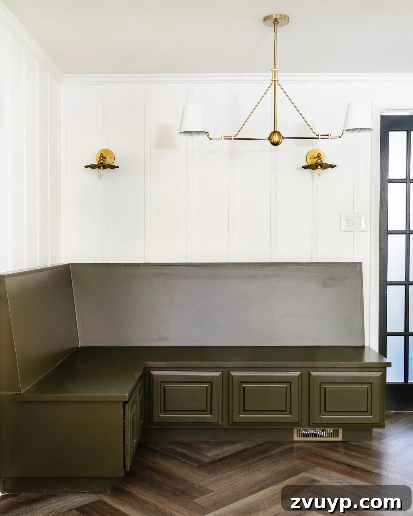 DIY Batten Wall Hack: Lattice Strips for an Affordable Look 12 A cozy breakfast nook featuring a rich green banquette bench, a pristine white batten wall meticulously crafted from lattice strips, and elegant brass lighting fixtures that illuminate the space, complementing the overall design.