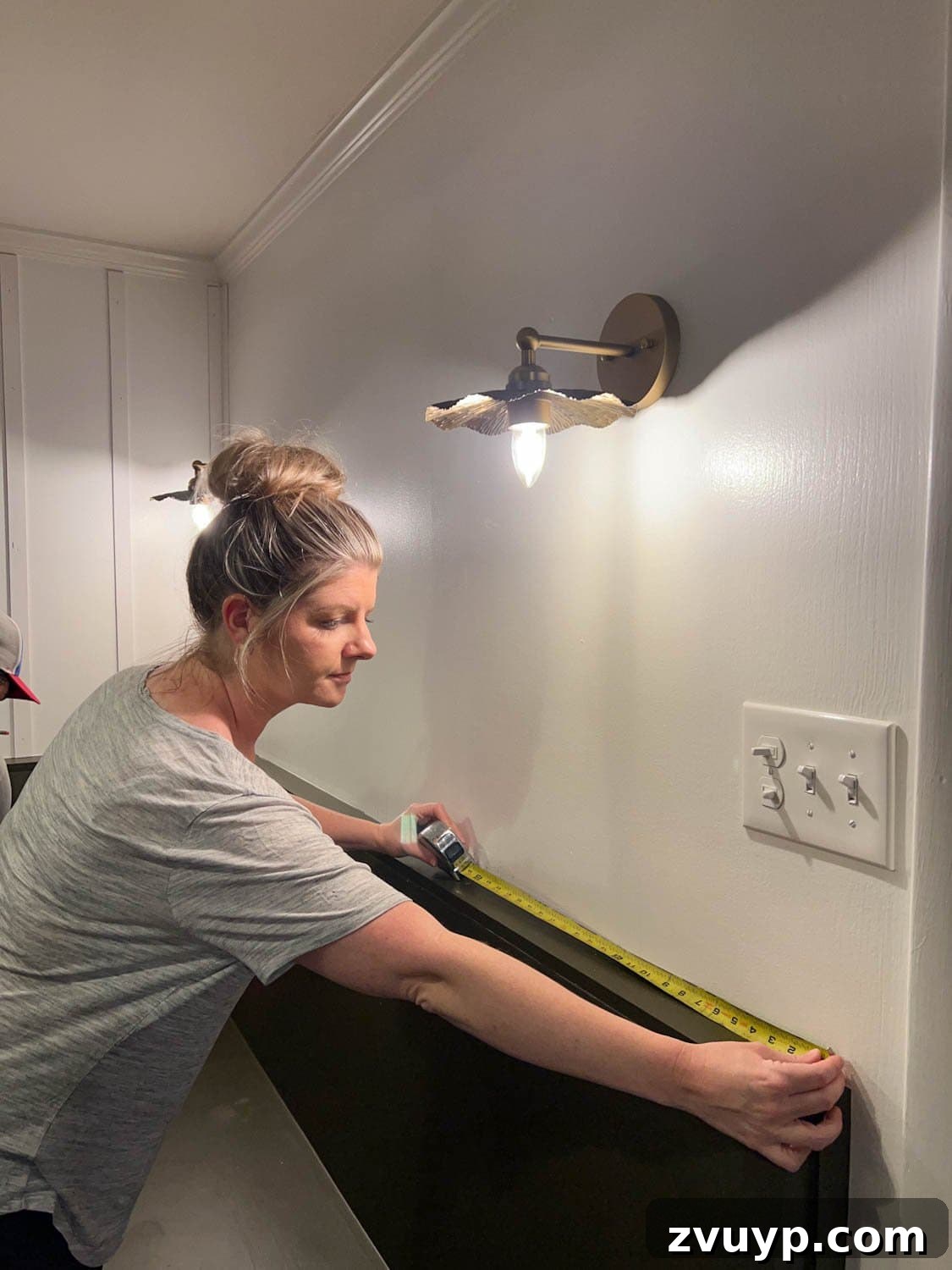 DIY Batten Wall Hack: Lattice Strips for an Affordable Look 5 A person meticulously measuring a wall with a tape measure to plan the placement of lattice strips for a DIY batten wall project, ensuring accurate spacing and layout.