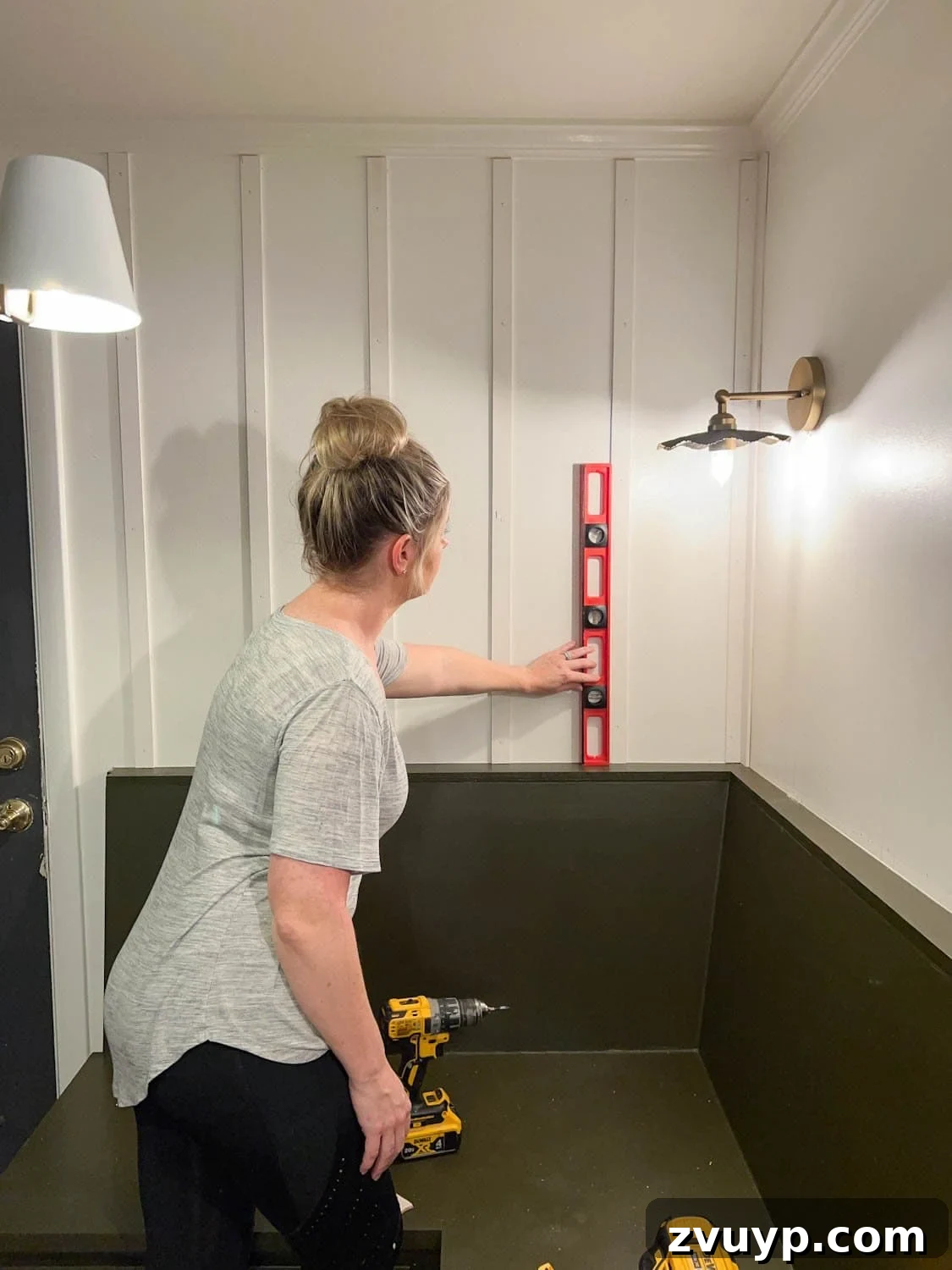 DIY Batten Wall Hack: Lattice Strips for an Affordable Look 6 A person using a level to ensure that a newly placed lattice strip for a DIY batten wall is perfectly perpendicular and straight against the wall.