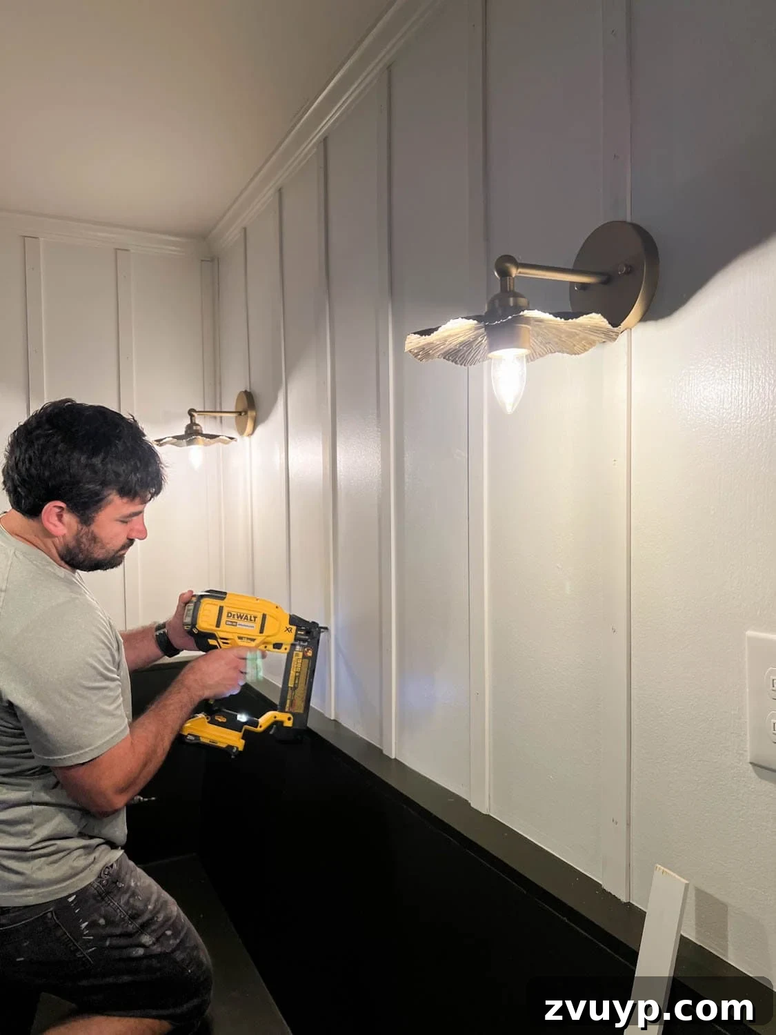 DIY Batten Wall Hack: Lattice Strips for an Affordable Look 8 A close-up view of a person using a brad nailer to secure lattice strips to a wall, effectively creating a DIY batten wall molding with precision and ease.