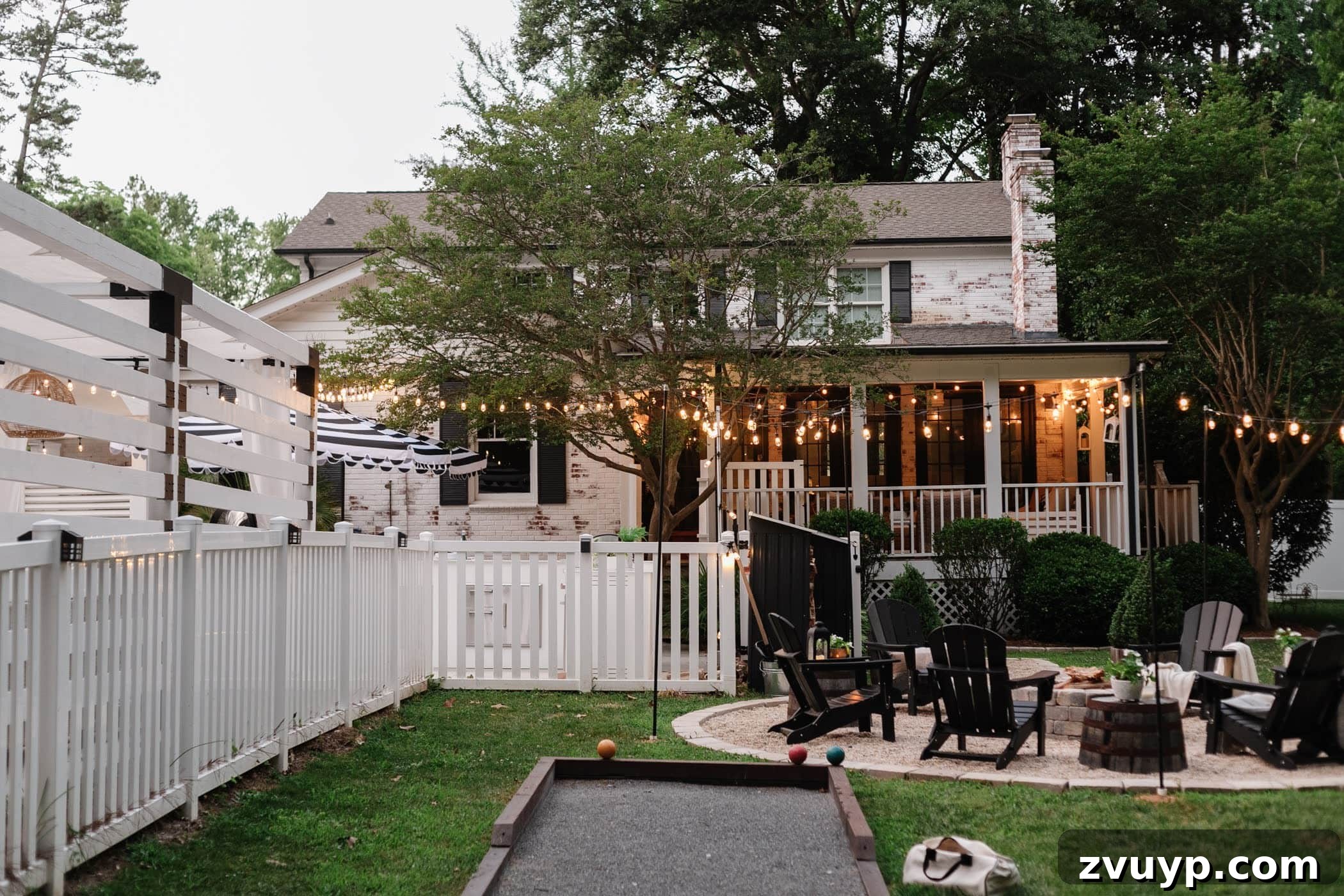 Our Home's Incredible 5-Year Transformation Tour 90 stunning limewashed brick house with a beautifully landscaped backyard featuring a cozy fire pit, a fun bocce ball court, a pristine white fence, an inviting back porch, and charming string lights, creating an ideal space for outdoor living and entertainment