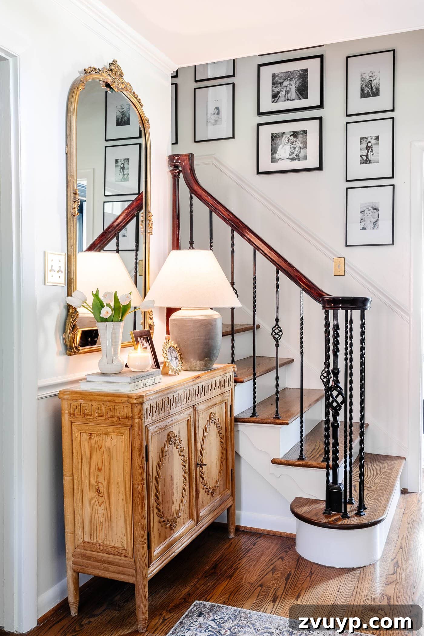 Our Home's Incredible 5-Year Transformation Tour 10 after foyer front entryway and stairs, featuring crisp white walls, a striking carved wood cabinet, and an ornate gold mirror, enhancing light and style