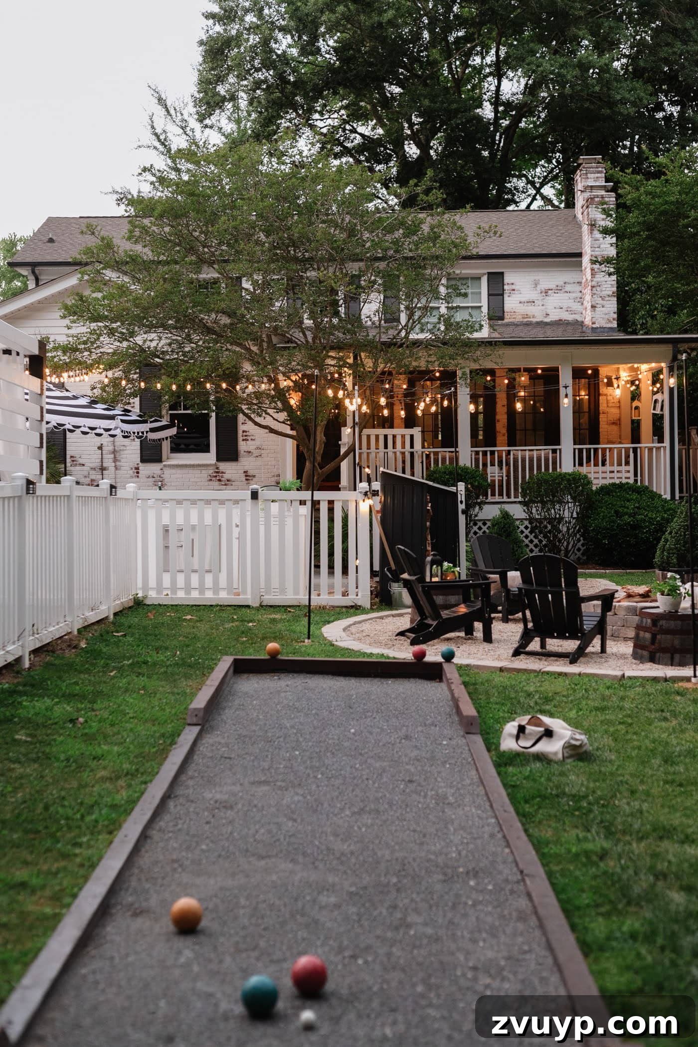 Our Home's Incredible 5-Year Transformation Tour 91 beautiful limewashed brick house with a meticulously landscaped backyard featuring a cozy fire pit, a playful bocce ball court, a pristine white fence, an inviting back porch, and charming string lights, creating a perfect blend of elegance and outdoor fun
