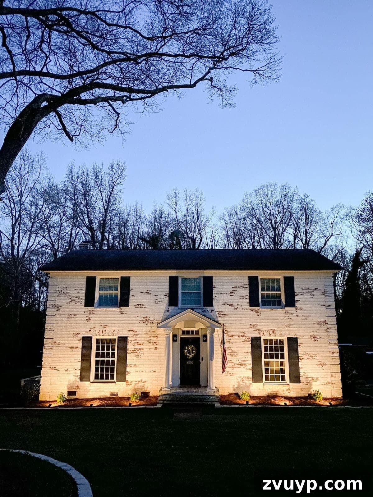 Our Home's Incredible 5-Year Transformation Tour 93 elegant limewashed brick colonial house illuminated by solar spotlights, enhancing its curb appeal at night