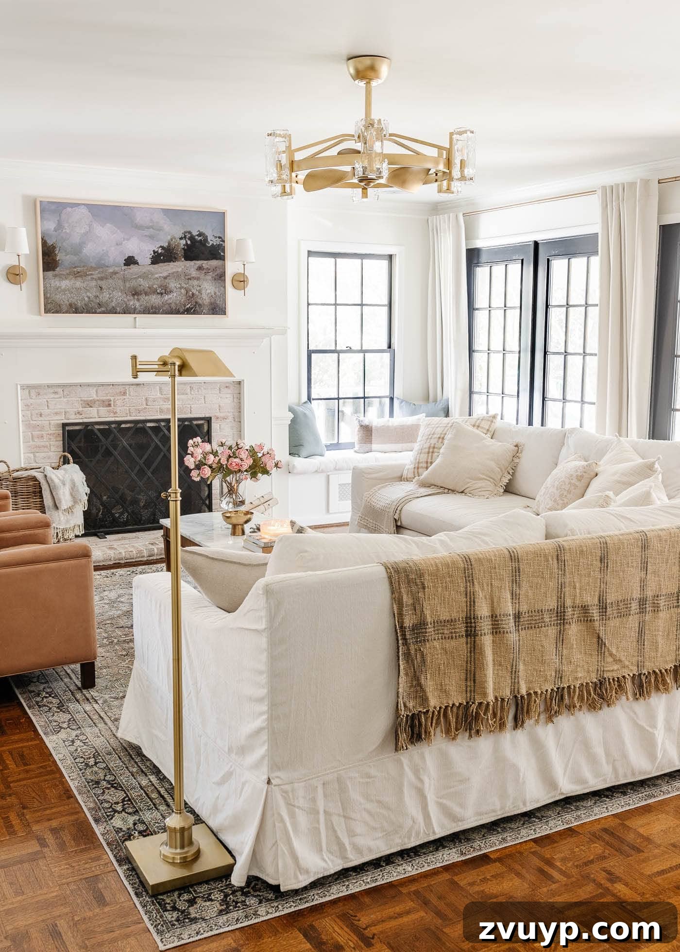 Our Home's Incredible 5-Year Transformation Tour 34 serene white living room showcasing a newly limewashed brick fireplace, a dazzling gold fandelier, plush white Pottery Barn sofas, cozy leather recliners, an integrated art TV, and elegant black French doors, all contributing to a modern and comfortable aesthetic