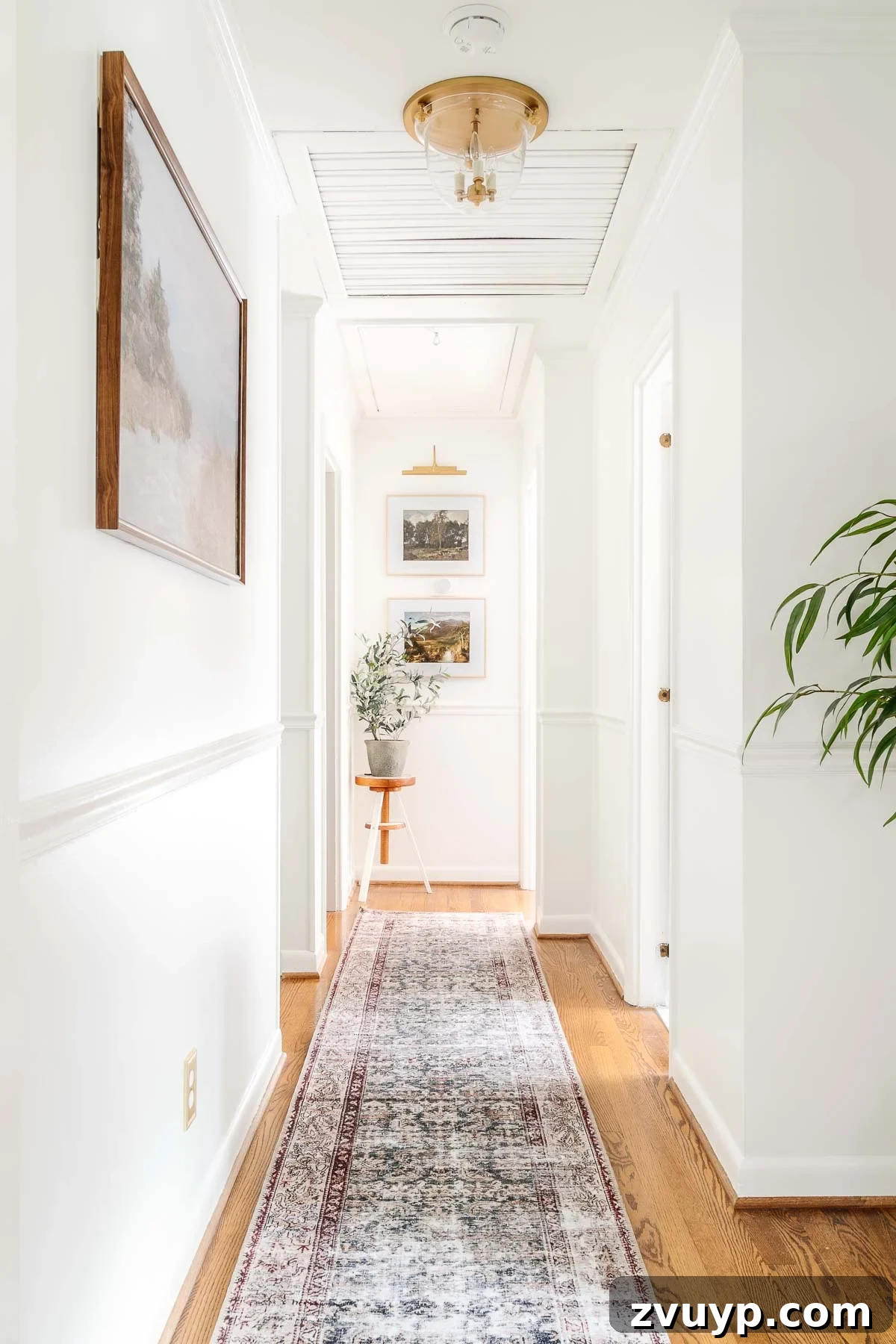 Our Home's Incredible 5-Year Transformation Tour 45 bright white hallway with contrasting black doors, a captivating vintage runner rug, an elegant brass light fixture, and charming landscape art, creating an inviting and stylish transitional space