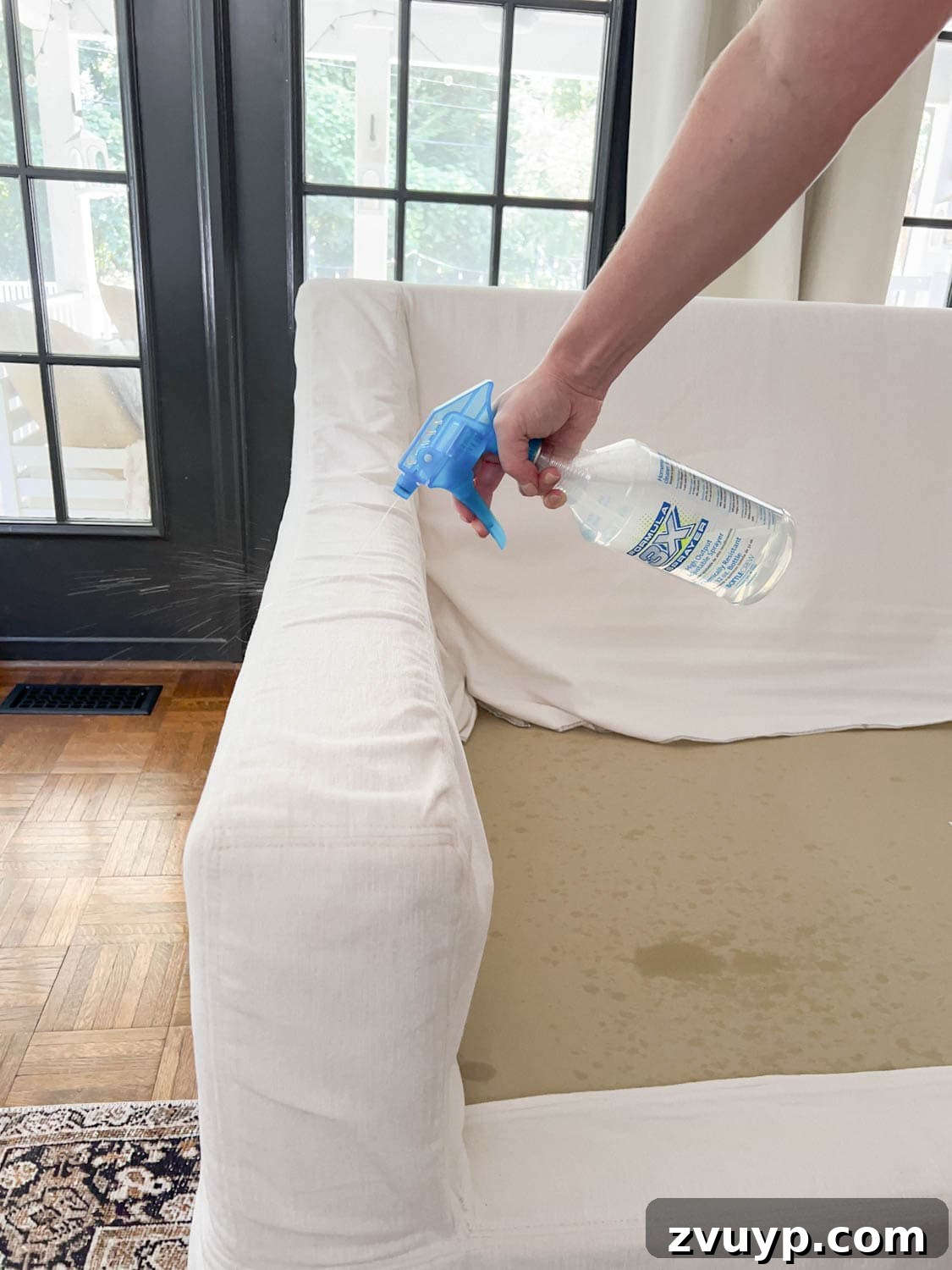Revive Your Fabric Furniture The Ultimate Upholstery Deep Clean 12 Person spraying a DIY couch cleaner onto the sofa fabric to remove dirt and grime.