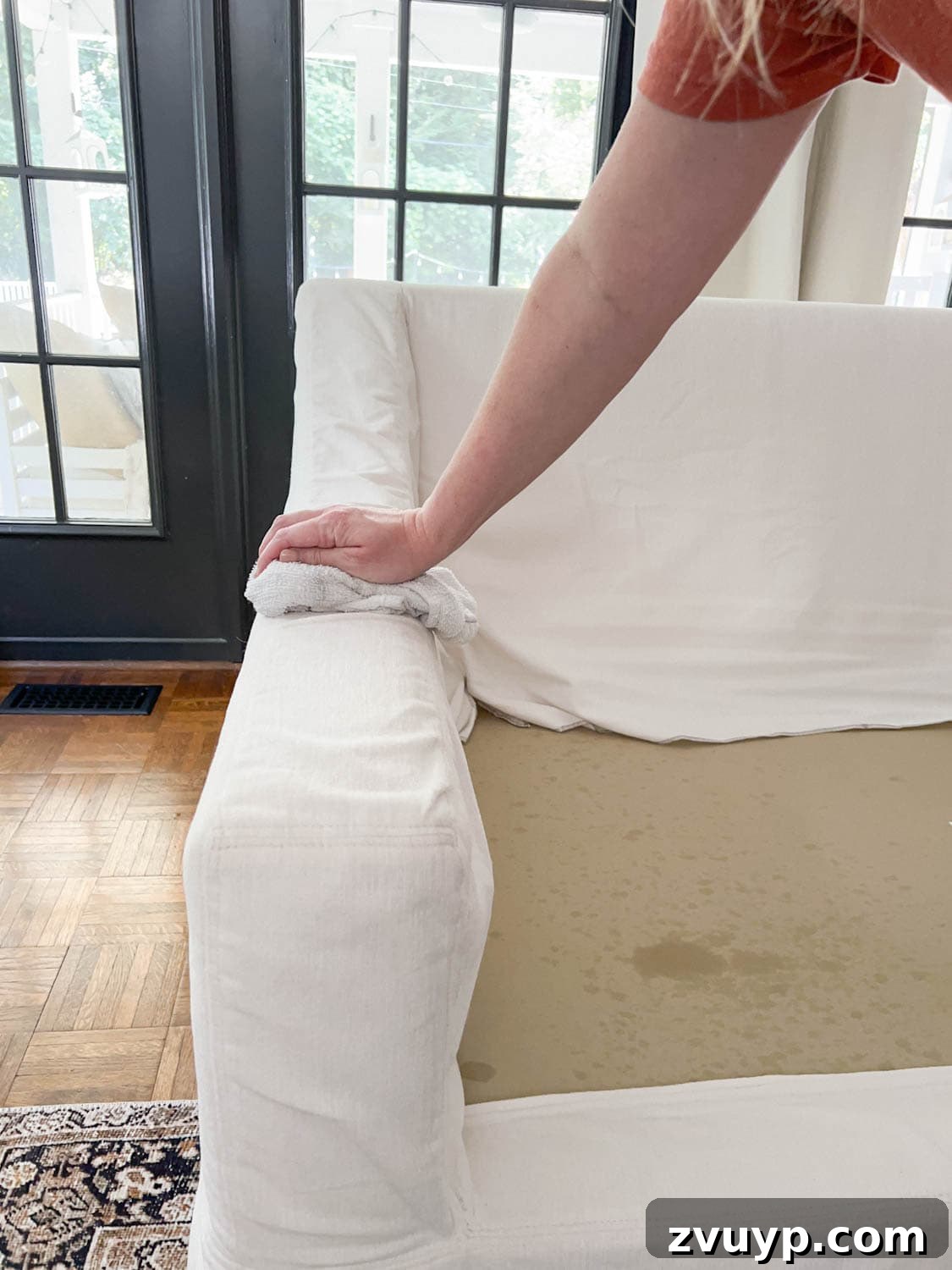 Revive Your Fabric Furniture The Ultimate Upholstery Deep Clean 13 A person wiping up DIY couch cleaner from upholstery to clean a sofa, revealing a cleaner surface.
