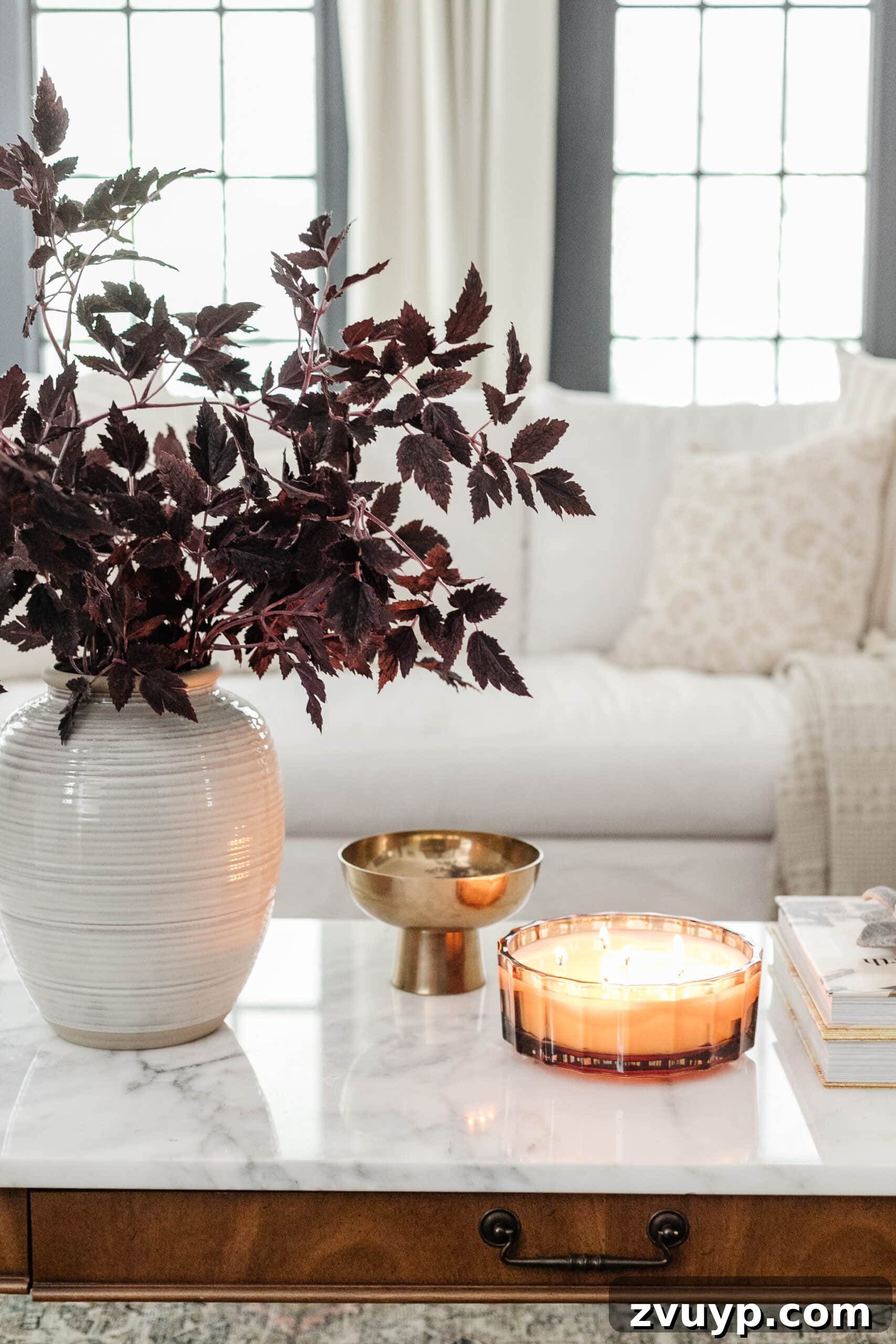 fall decor on a coffee table with vase of fall branches, candle, brass bowl, and books