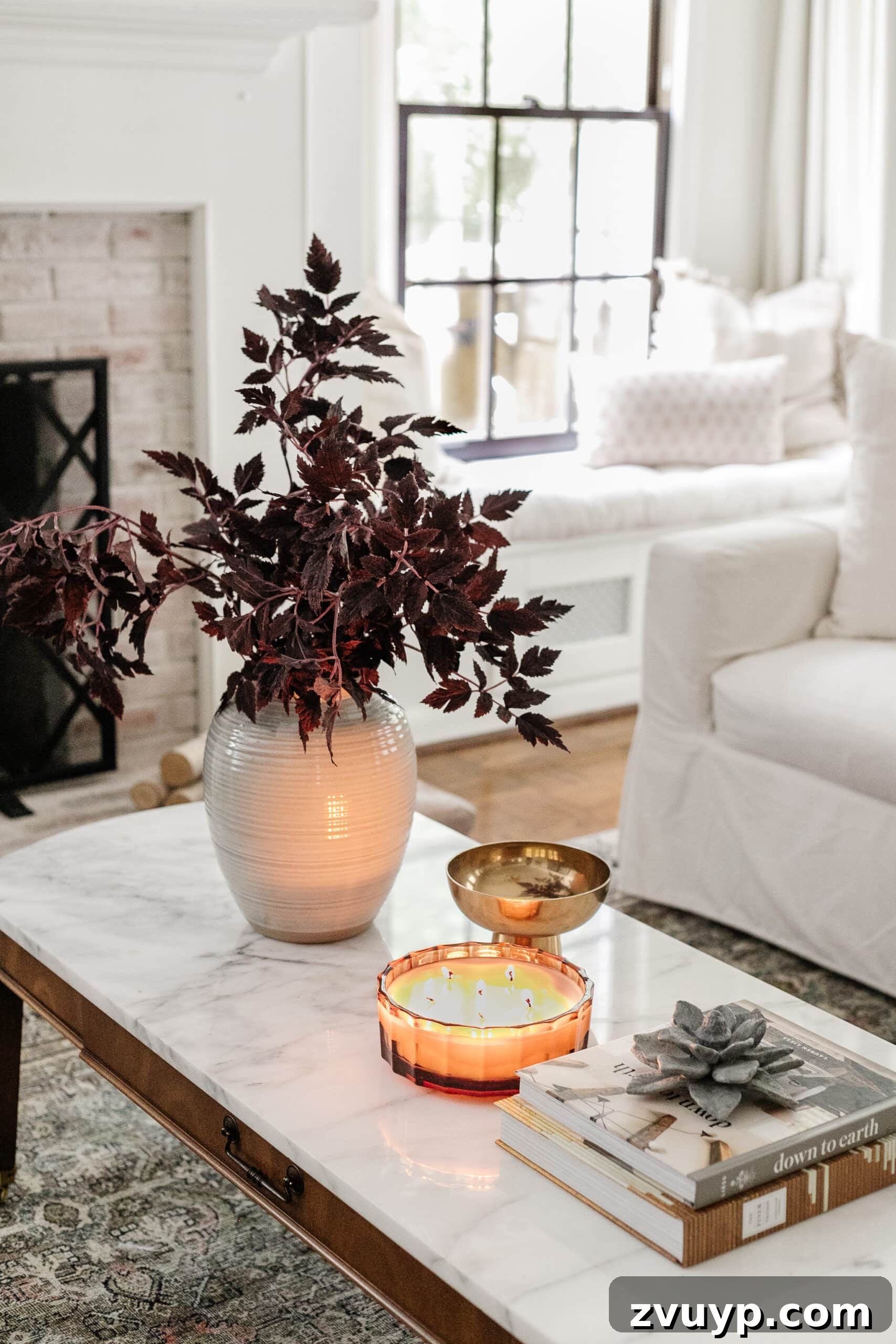 fall decor on a coffee table with vase of fall branches, candle, brass bowl, and books