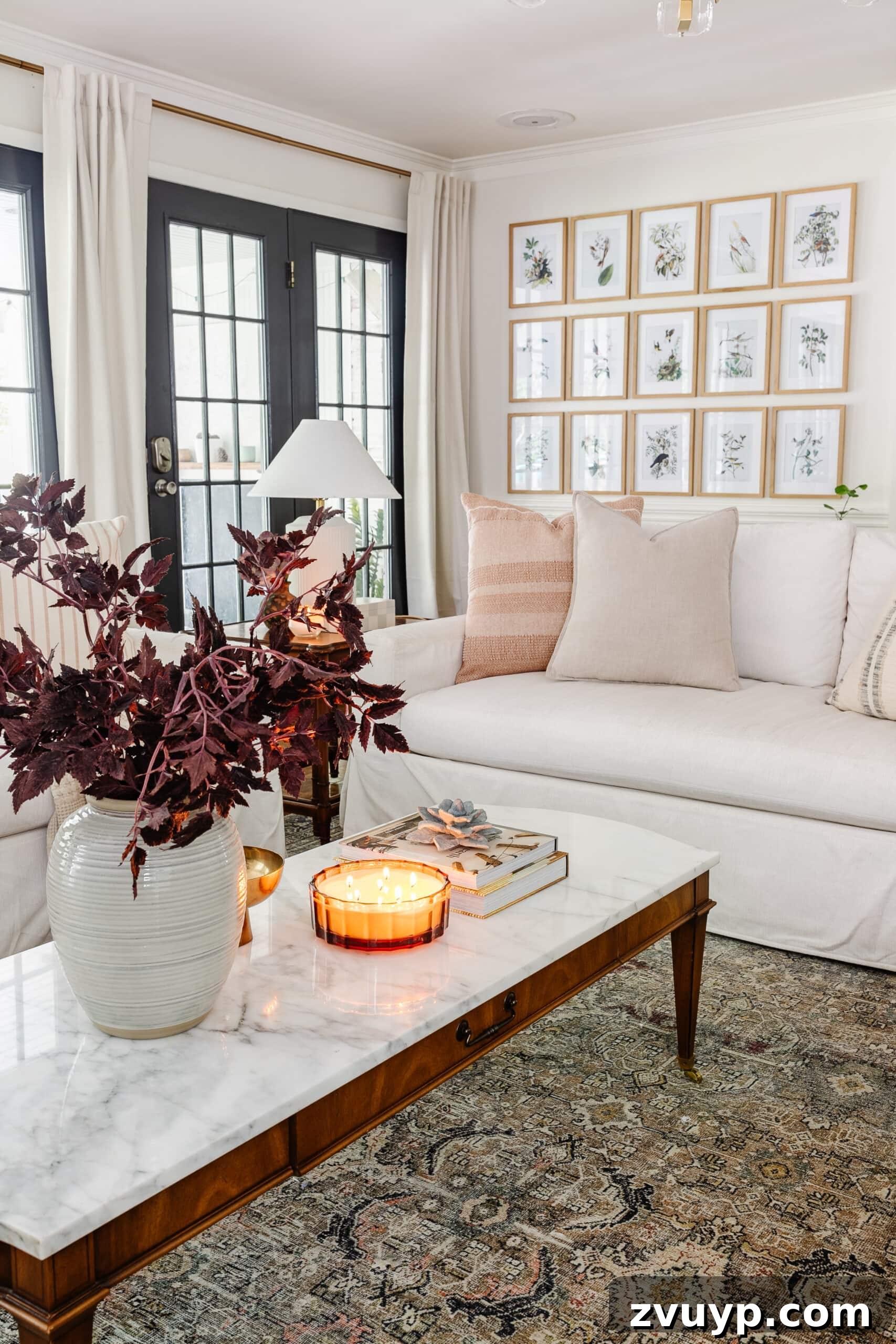 coffee table fall decor with vase of fall stems, candle, bowl, and books in front of white sofa with neutral pillows