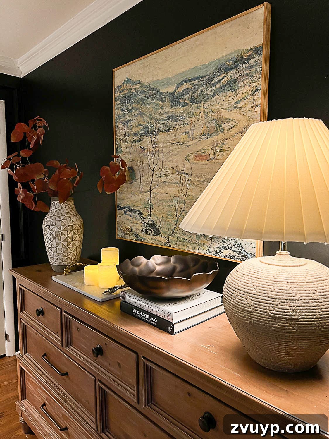 Sweet Dreams on a Budget: 10 Cozy Bedroom Tips for Ultimate Rest 11 A cozy bedroom dresser styled with elegant fall branches in a vase, realistic flameless candles, and a warm table lamp, creating an inviting and tranquil atmosphere.