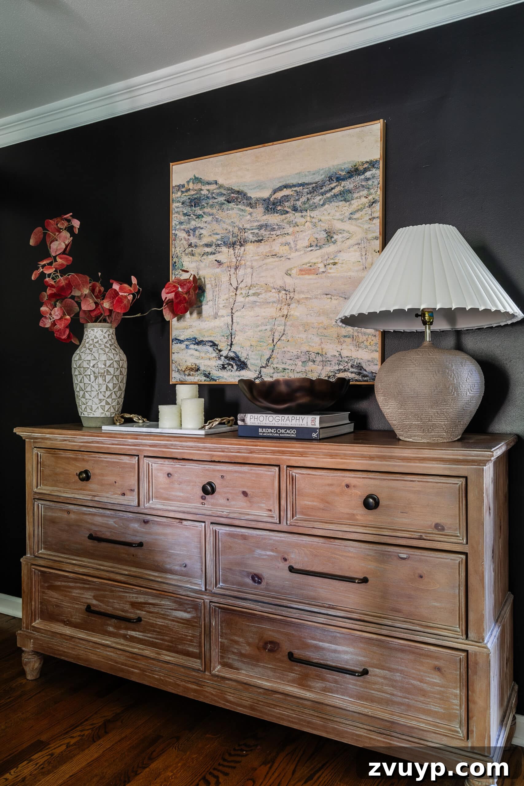 Sweet Dreams on a Budget: 10 Cozy Bedroom Tips for Ultimate Rest 4 An elegant wooden dresser adorned with substantial wall art, a vase brimming with autumnal branches, and a stylish table lamp, creating a cozy and curated bedroom vignette.