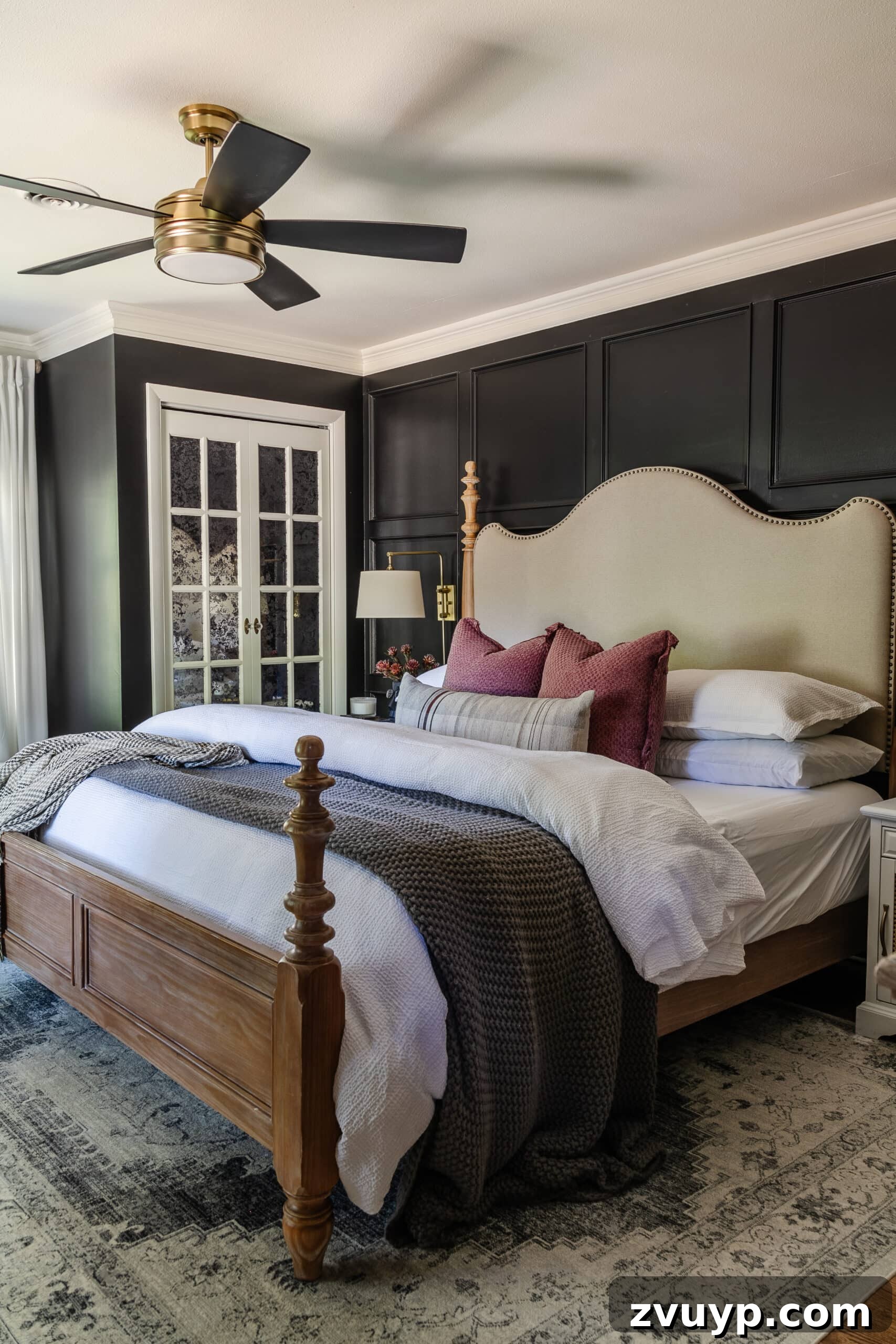 Sweet Dreams on a Budget: 10 Cozy Bedroom Tips for Ultimate Rest 5 A luxurious bedroom featuring dark black walls, lavish fluffy bedding, an elegant wood and upholstered bed, and a sleek ceiling fan, combining comfort with modern style.