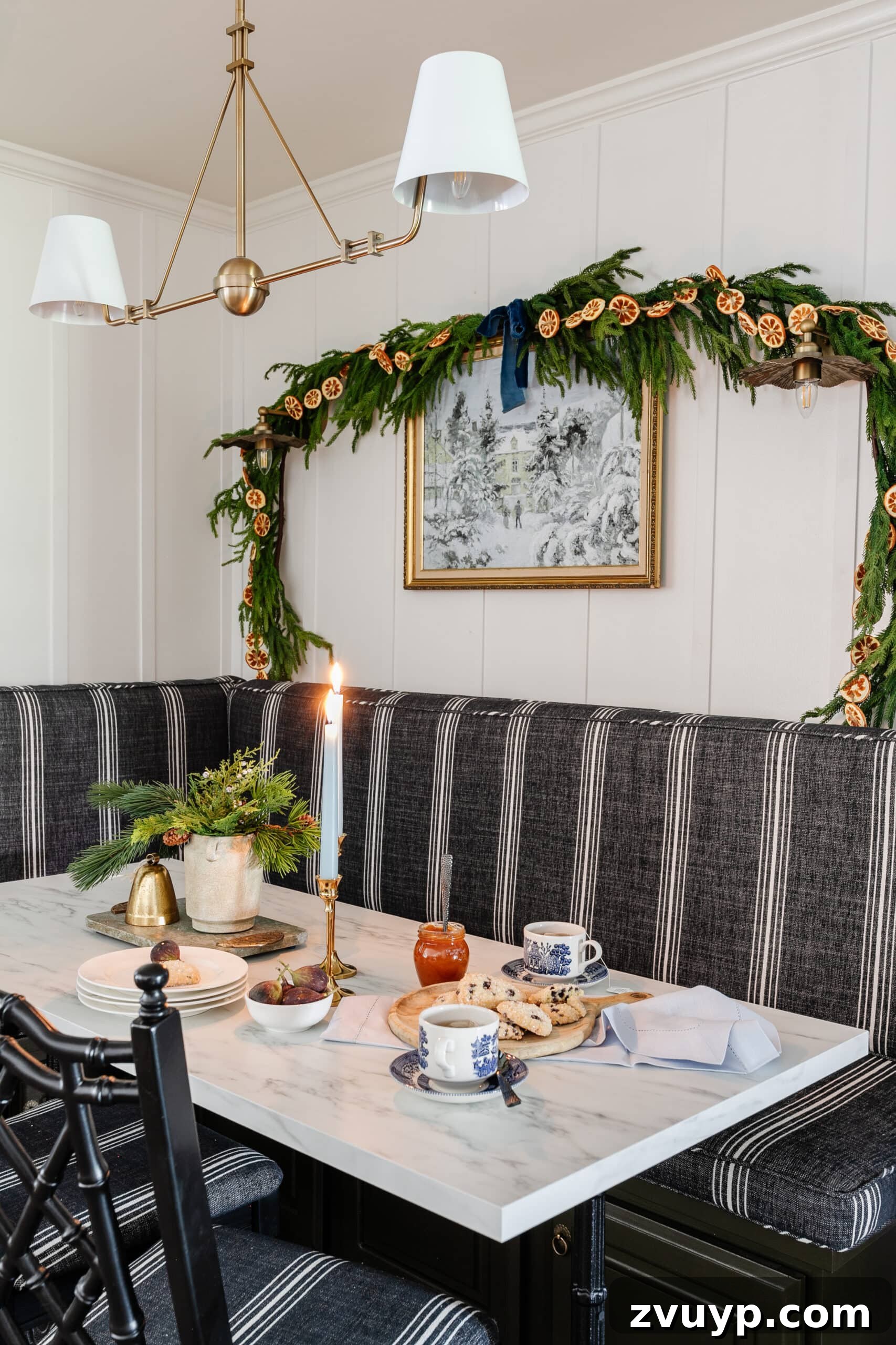 Free Printable Winter Art for Instant Home Decor 5 Serene winter scene painting adorning a breakfast nook wall, beautifully framed and enhanced with delicate pine and orange garland for a festive yet cozy ambiance.