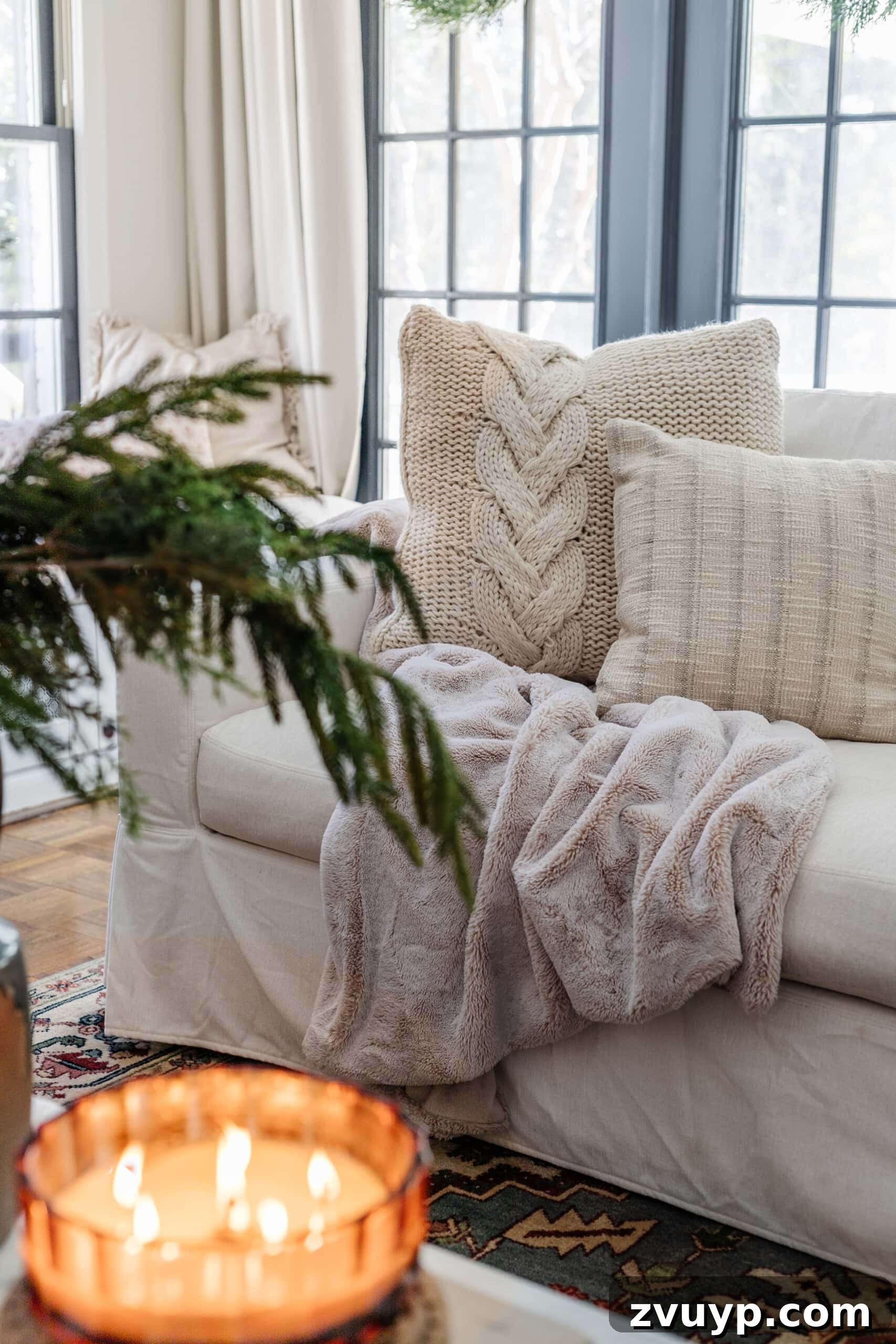 Warm Up Your Home 16 Cozy January Decor Essentials 2 winter home decor in a living room with faux fur blanket, knit pillows, green branches, and candles