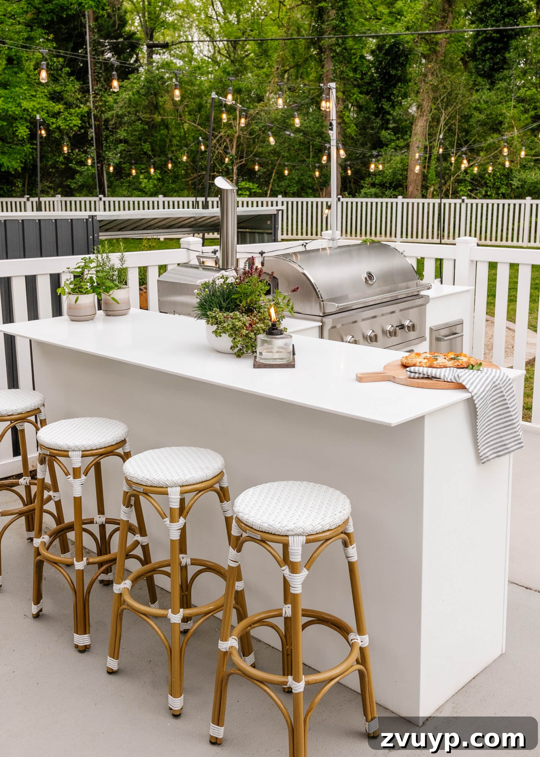 Effortless Spring Patio Refresh 8 white outdoor kitchen with grill, bar stools, string lights, white fence, and potted plants
