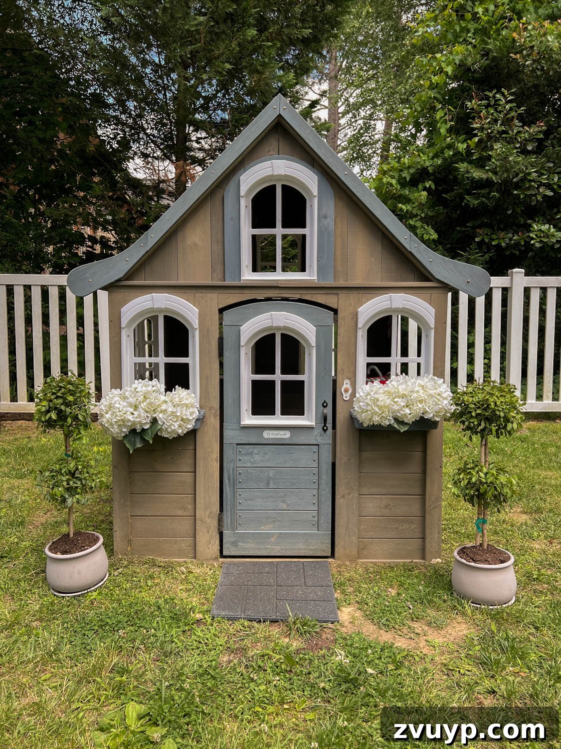Transform Your Side Yard: 8 Play Area & Trampoline Design Ideas 11 wooden outdoor playhouse with white flowers and topiaries, looking inviting
