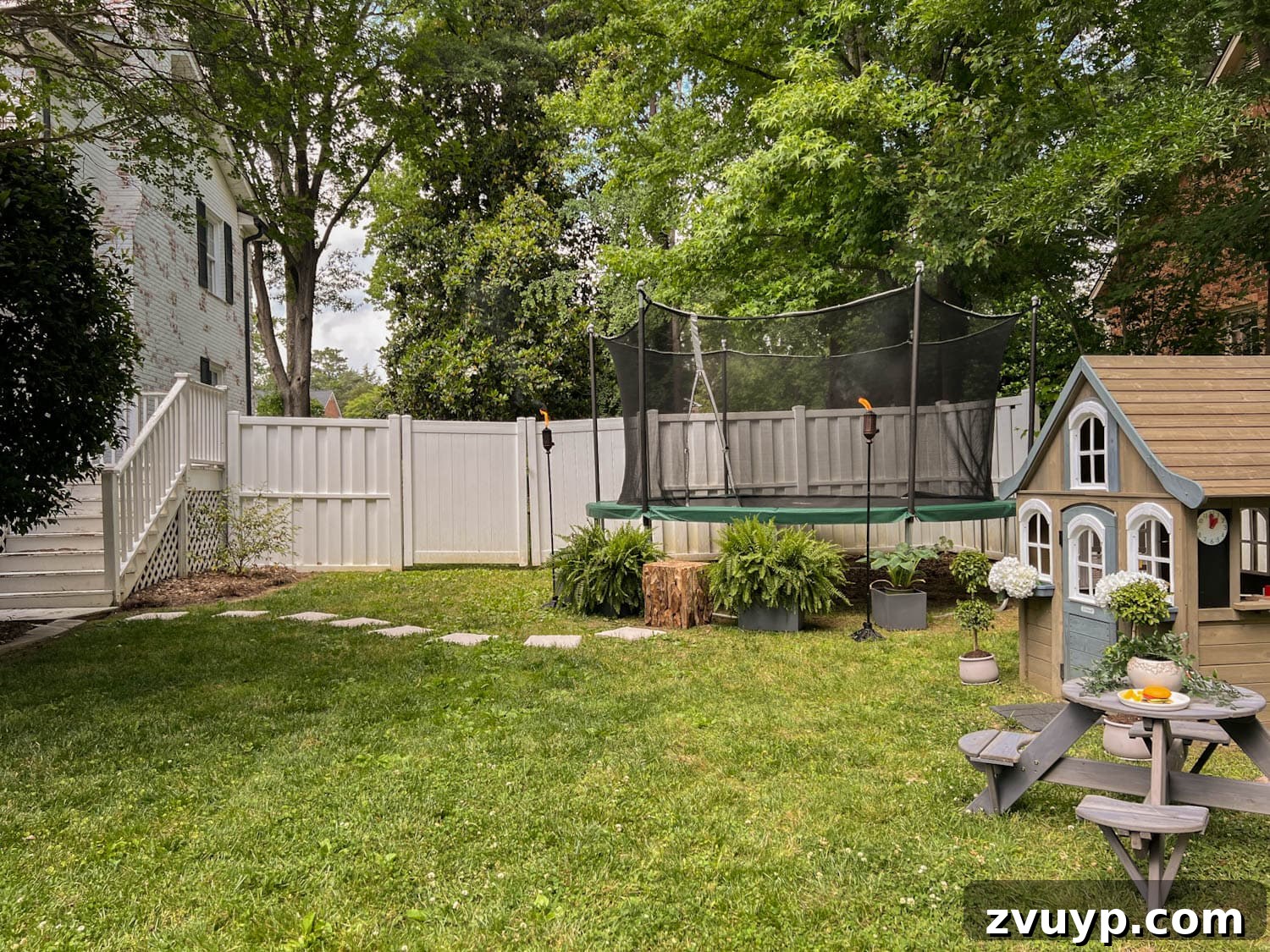 Transform Your Side Yard: 8 Play Area & Trampoline Design Ideas 8 side yard play area for kids with outdoor playhouse and trampoline, illuminated by tiki torches
