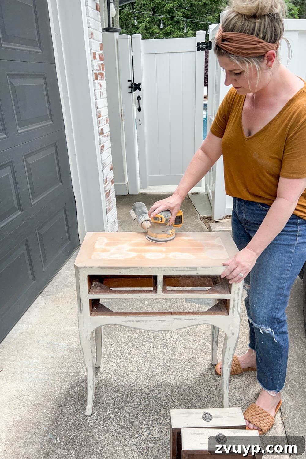DIY Bedside Table Refresh: Secrets to Smooth Gloss Paint 4 sanding a bedside table with an orbital sander to remove distressed paint and create a smooth surface