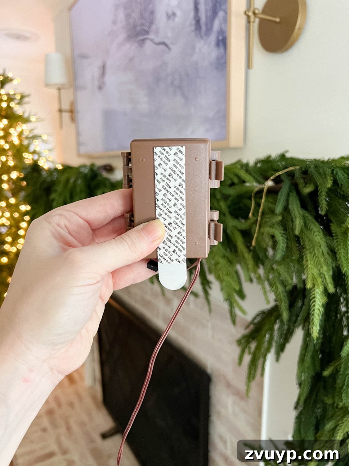 Craft Your Own Stunning Christmas Mantel Garland 8 Detailed shot of a fairy light battery pack being attached to a mantel with a Command strip for hidden setup.