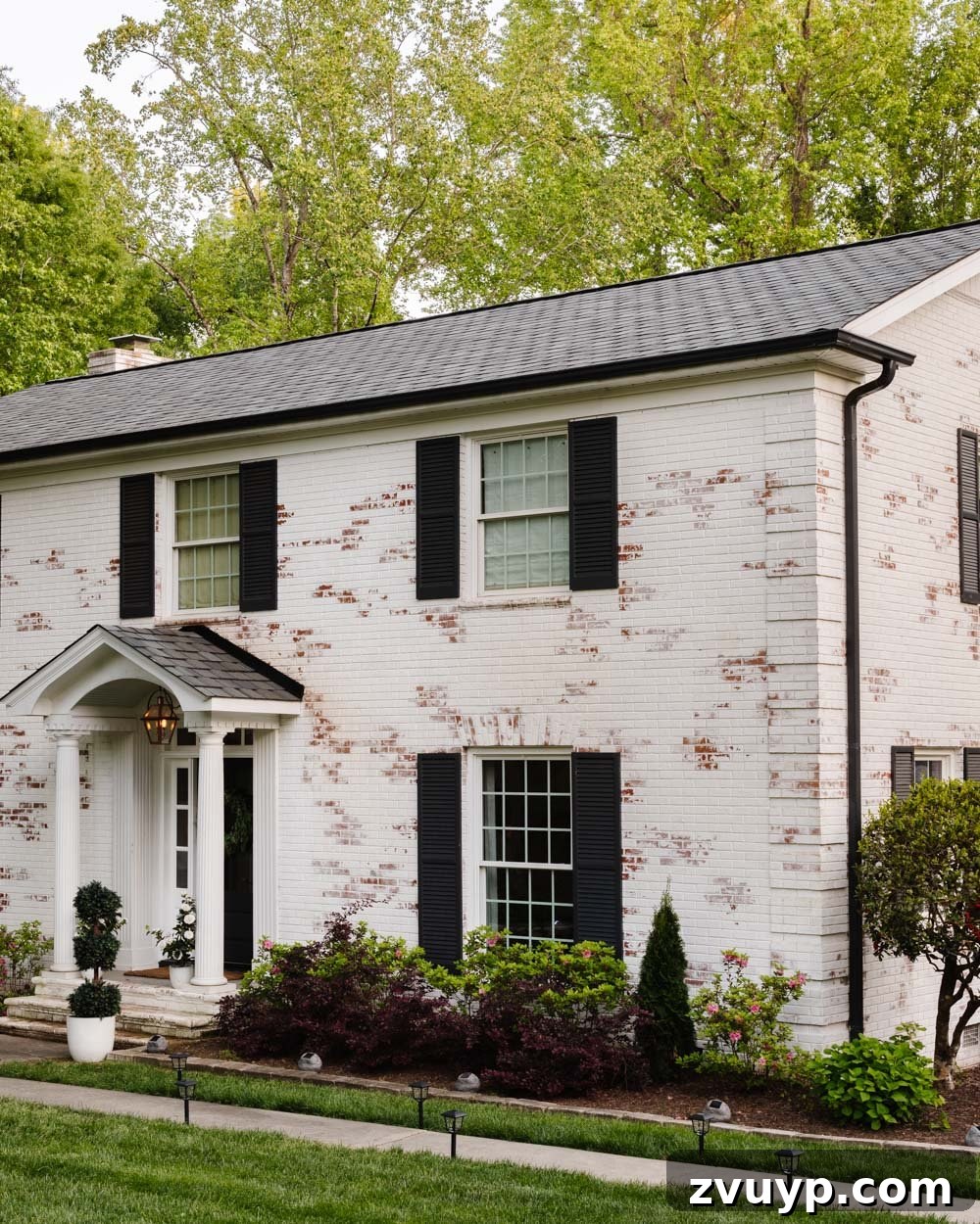 Limewashed brick colonial home with elegant designer shingles and modern solar lighting.