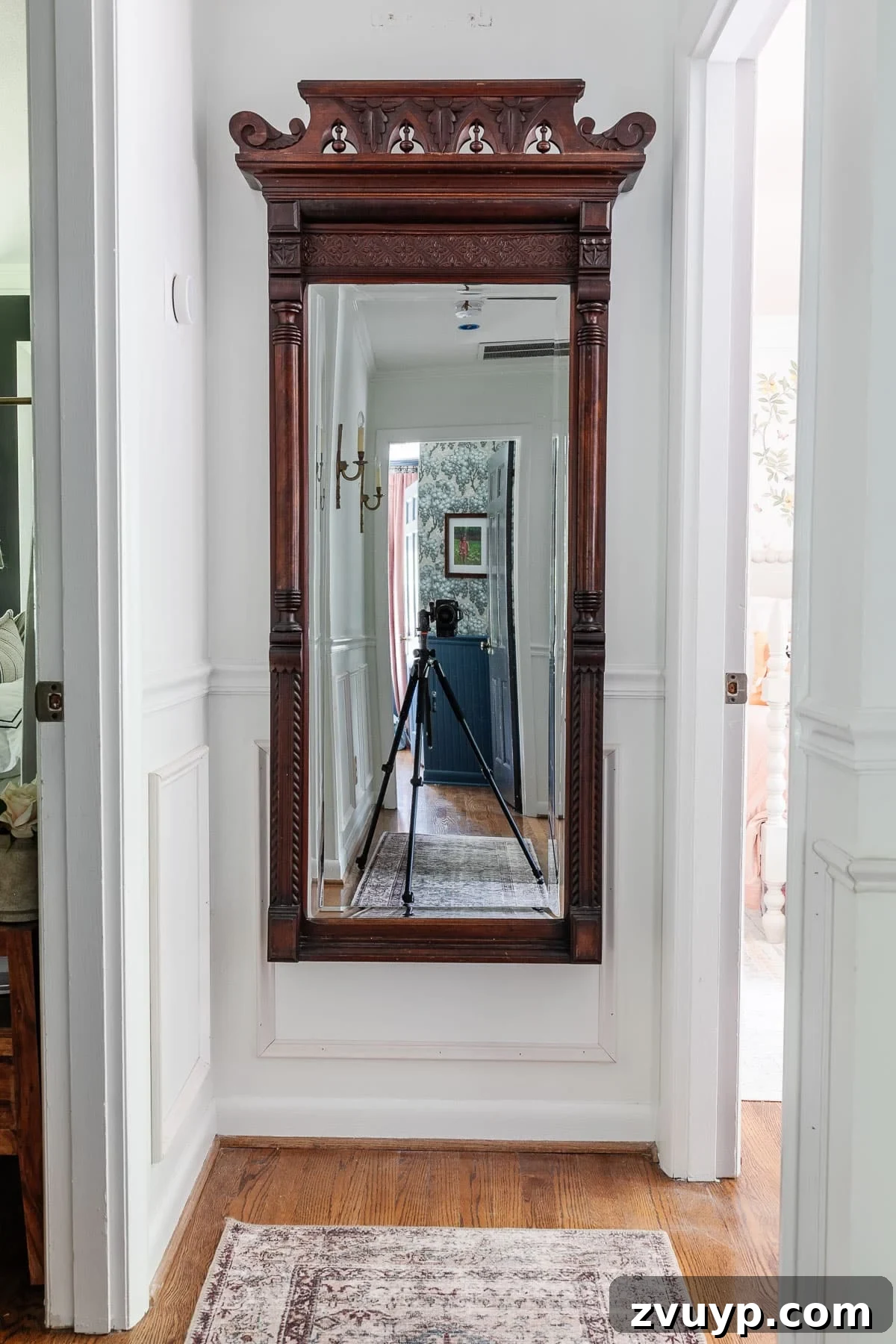 From Concept to Hallway Reality 6 Ornate antique mirror with a dark wooden frame hanging in a hallway with wainscoting.