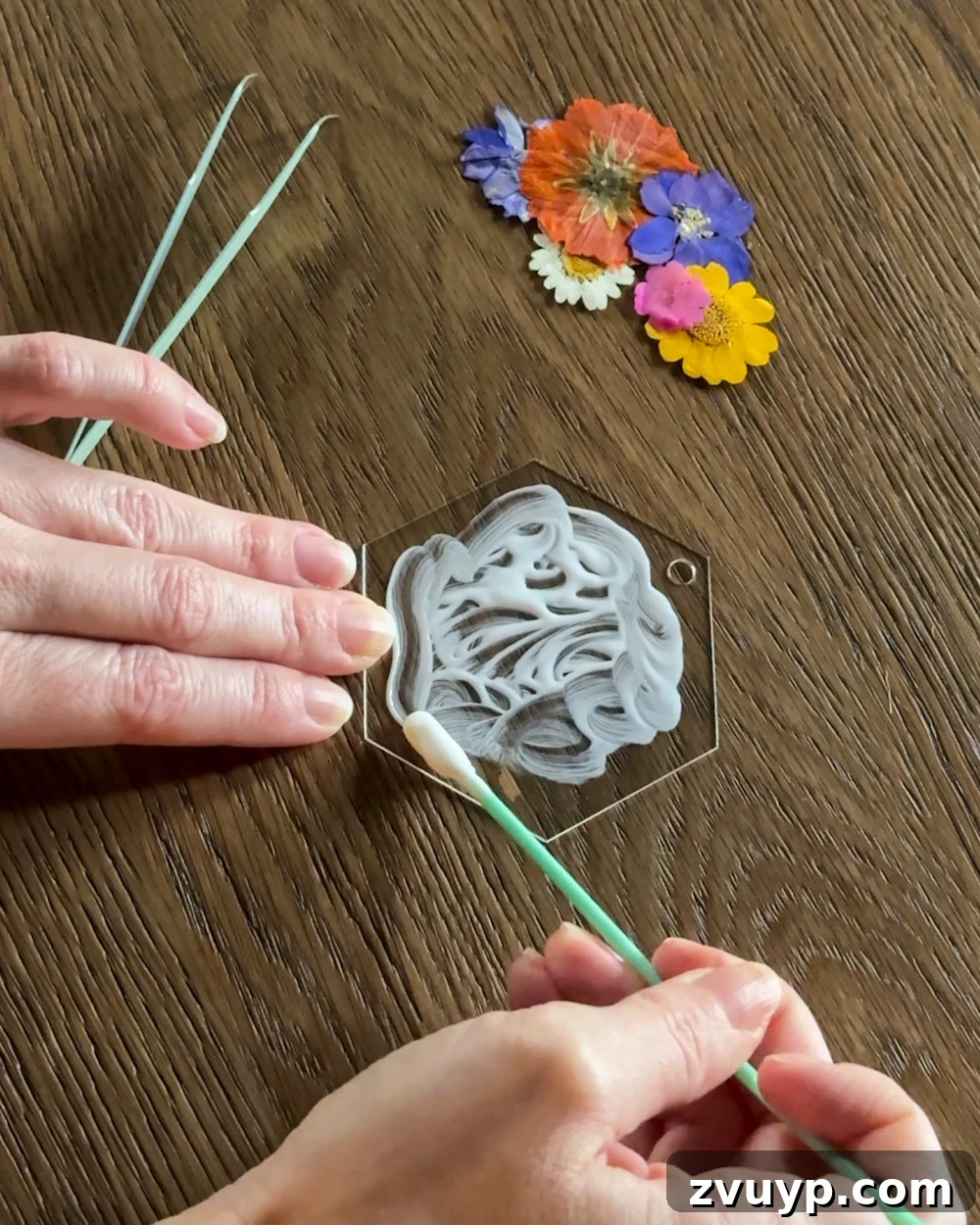Surprisingly Simple Pressed Flower Ornaments 5 A person arranging various colorful pressed flowers onto a clear acrylic tag to plan the design for a DIY Christmas ornament, demonstrating Step 1 of the crafting process.