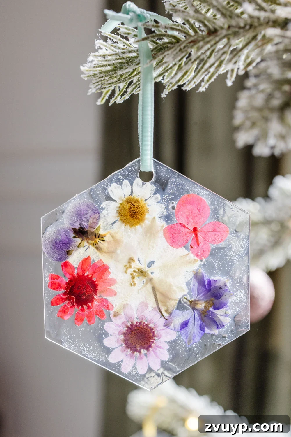 Surprisingly Simple Pressed Flower Ornaments 8 A finished DIY pressed flower ornament with a delicate ribbon loop, held up to show its readiness to hang on a Christmas tree. The ornament beautifully showcases colorful pressed flowers.